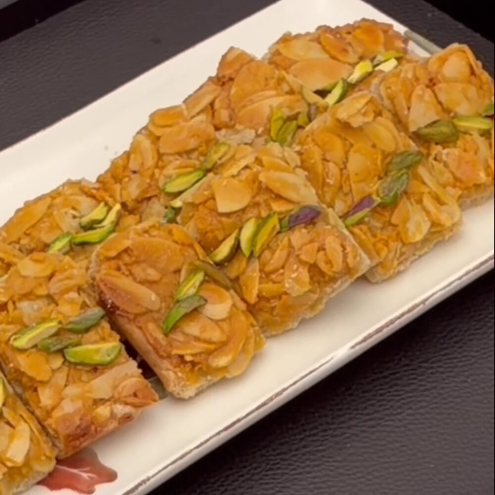 Almond Queen squares topped with toasted sliced almonds and a pistachio garnish on a white serving tray, Honey & Fig Bakery, Pflugerville, Texas