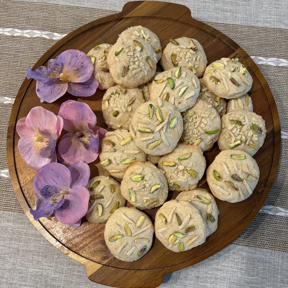 Tabrizi Cookies topped with slivered almonds and pistachio on a round wooden board with orchids, Honey & Fig Bakery, Pflugerville, Texas
